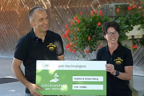 Ein Mann und eine Frau halten eine Auszeichnung mit dem Titel "1. Platz Projekt Nachhaltigkeit".